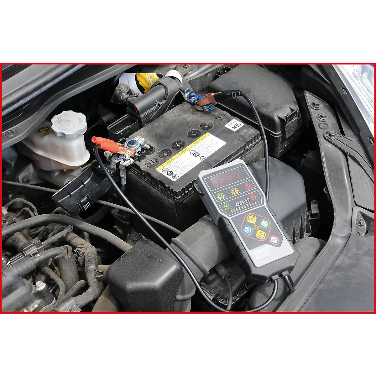 Ein Autobatterietester mit angeschlossenen Klemmen an einer Autobatterie. Der Motorraum ist geöffnet.